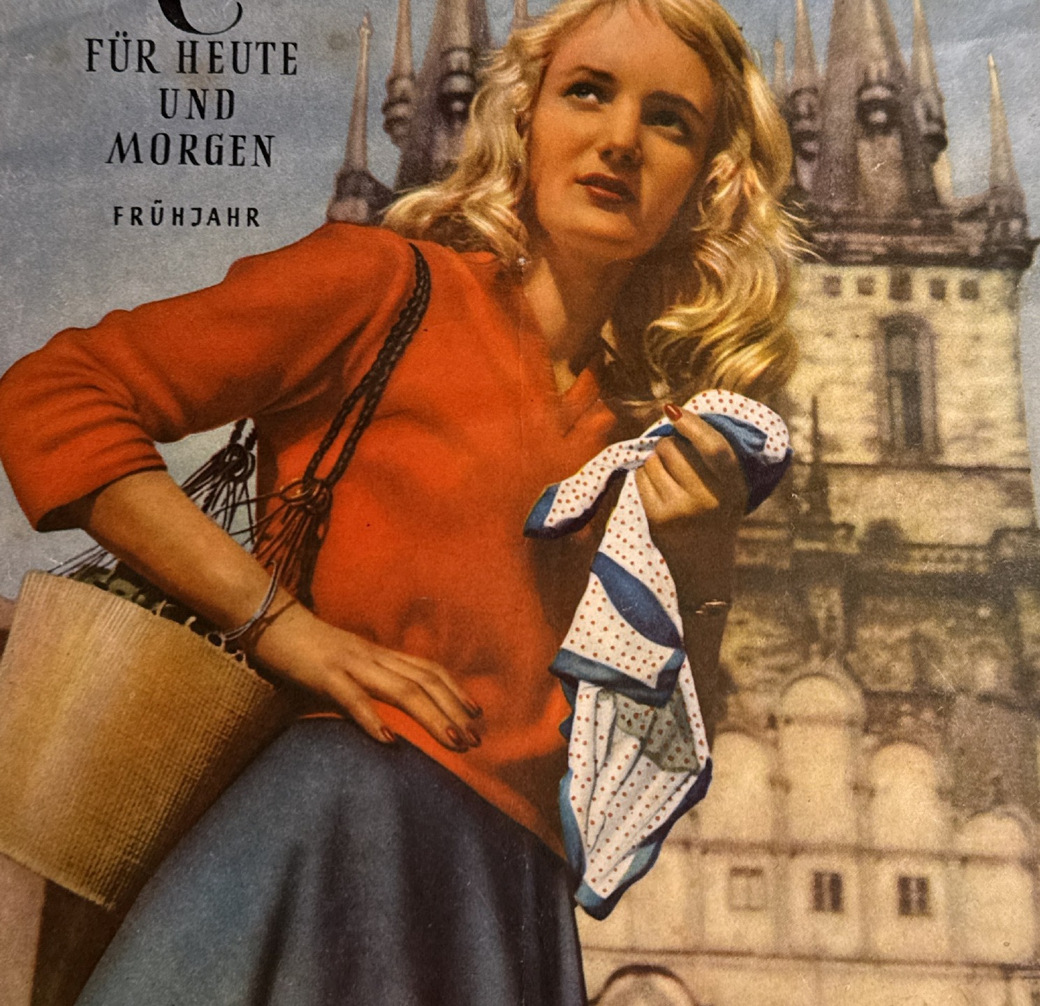 Detail of blonde model in coral V-neck sweater with straw bag before Leipzig Neues Rathaus